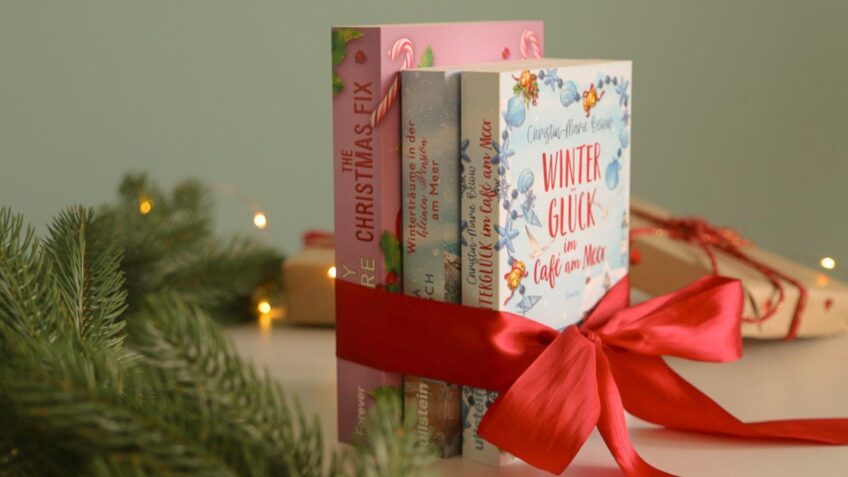 Drei weihnachtlich gestaltete Bücher als Geschenkpaket mit roter Schleife, umgeben von Tannenzweigen und warmen Lichterketten.